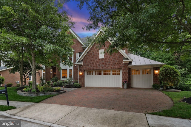 view of front of house featuring decorative driveway, a standing seam roof, brick siding, an attached garage, and metal roof