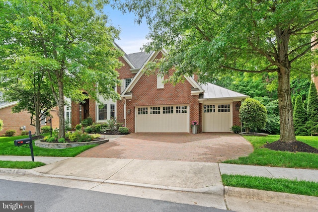 view of front of home featuring decorative driveway, brick siding, a standing seam roof, and a garage