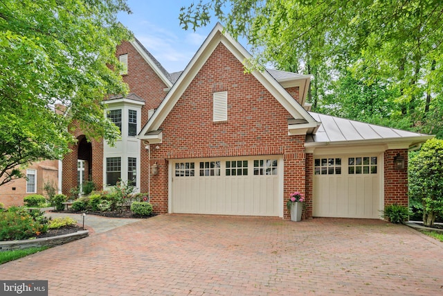 traditional home featuring decorative driveway, brick siding, a standing seam roof, a garage, and metal roof