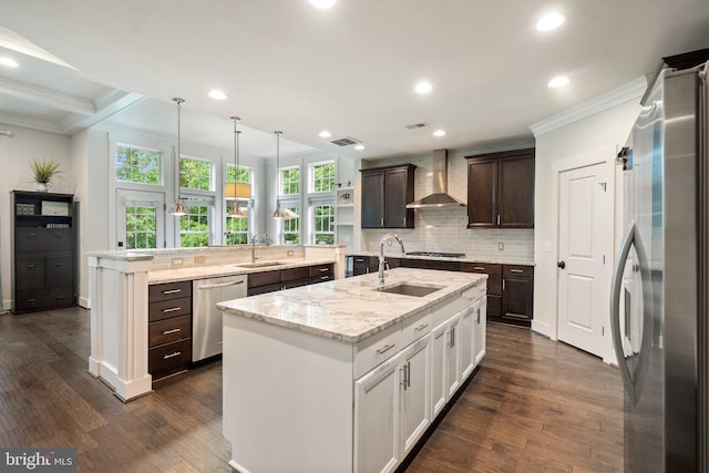 kitchen with stainless steel appliances, wall chimney exhaust hood, a center island with sink, crown molding, and a sink