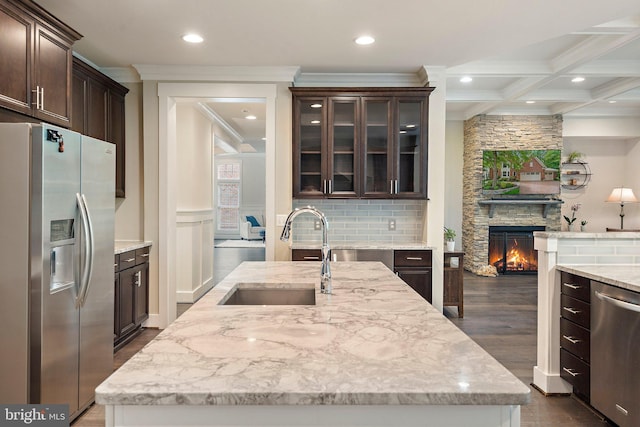 kitchen with appliances with stainless steel finishes, a sink, crown molding, a stone fireplace, and dark brown cabinetry
