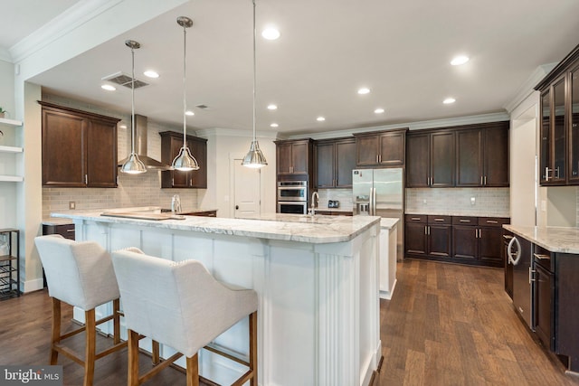 kitchen featuring a spacious island, ornamental molding, wall chimney exhaust hood, appliances with stainless steel finishes, and dark brown cabinetry