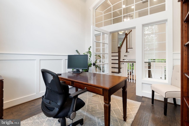office with dark wood finished floors, wainscoting, a decorative wall, and a towering ceiling