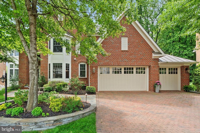 traditional-style house with a standing seam roof, decorative driveway, brick siding, and metal roof