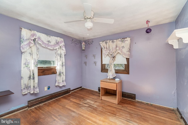 empty room featuring ceiling fan, baseboard heating, and wood finished floors
