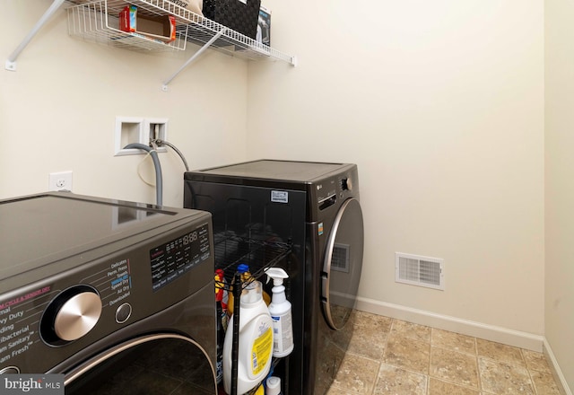 clothes washing area with laundry area, visible vents, washing machine and dryer, baseboards, and stone finish floor