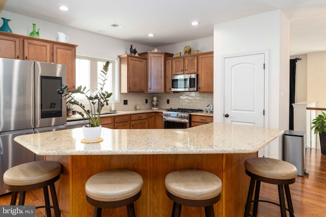 kitchen with light wood-style floors, appliances with stainless steel finishes, tasteful backsplash, and brown cabinets