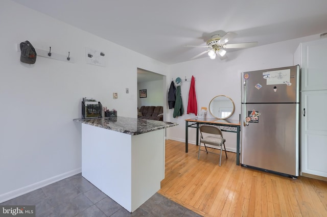 kitchen with white cabinets, ceiling fan, freestanding refrigerator, a peninsula, and dark stone counters
