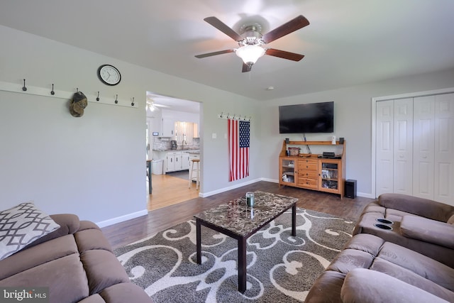 living area with baseboards, a ceiling fan, and dark wood finished floors