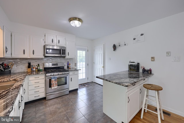 kitchen with appliances with stainless steel finishes, backsplash, a peninsula, and white cabinetry