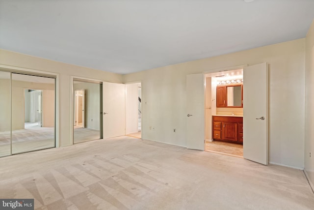 unfurnished bedroom with baseboards, multiple closets, light carpet, and ensuite bathroom