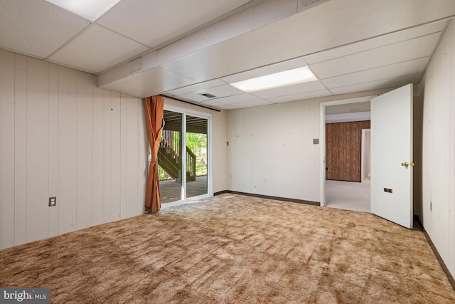 carpeted spare room featuring wooden walls, visible vents, and a paneled ceiling