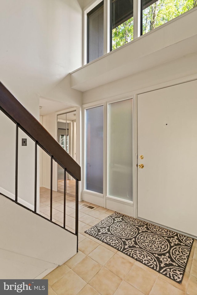 entrance foyer featuring stairway, light tile patterned floors, and a towering ceiling