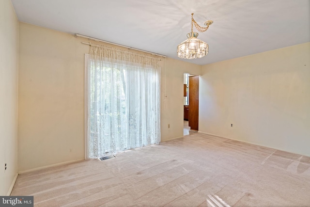 carpeted empty room featuring an inviting chandelier and visible vents
