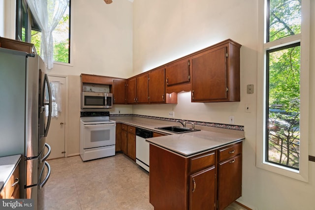 kitchen with a towering ceiling, brown cabinets, a sink, a peninsula, and stainless steel appliances