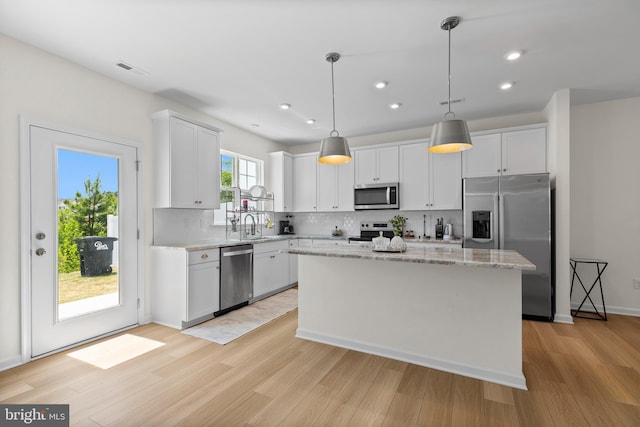 kitchen featuring decorative backsplash, light stone countertops, a center island, light wood finished floors, and stainless steel appliances