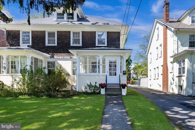 view of front of property with entry steps, a shingled roof, a sunroom, and a front lawn