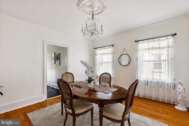 dining area with light wood-type flooring, ornamental molding, baseboards, and a chandelier
