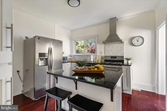 kitchen with wall chimney range hood, crown molding, appliances with stainless steel finishes, dark wood-style floors, and a breakfast bar