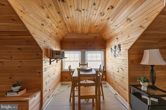 dining room with light wood-style floors, wood walls, baseboards, wooden ceiling, and vaulted ceiling