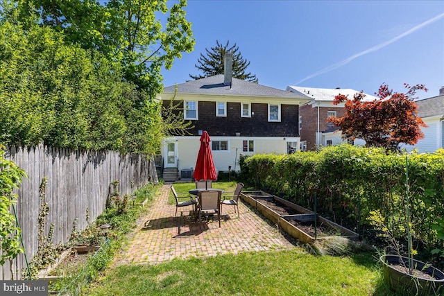 rear view of house featuring a patio, a fenced backyard, a yard, and a vegetable garden