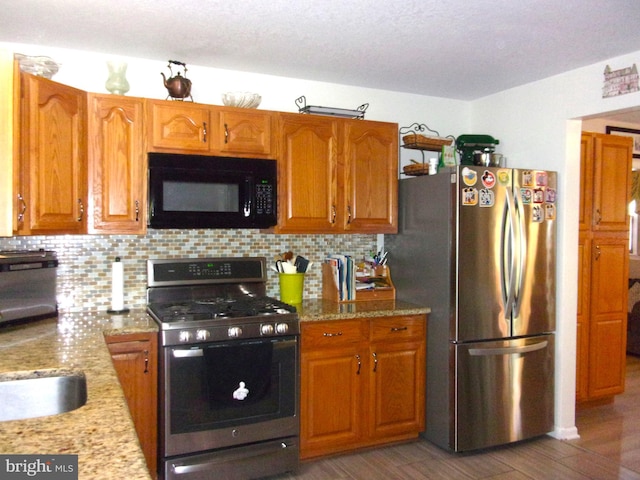 kitchen with brown cabinetry, decorative backsplash, appliances with stainless steel finishes, and light stone countertops
