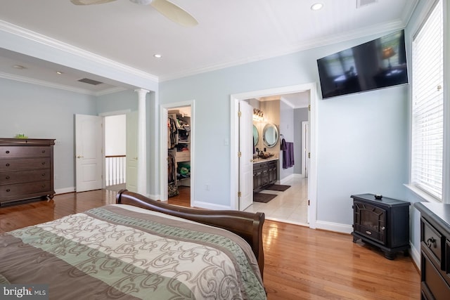 bedroom with a walk in closet, light wood finished floors, a wood stove, visible vents, and ornamental molding