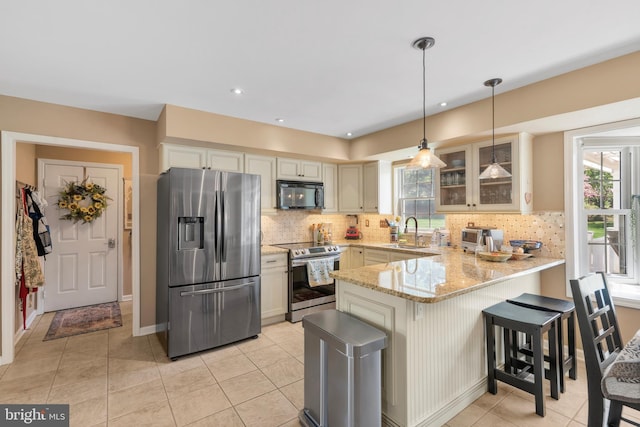 kitchen with appliances with stainless steel finishes, light stone counters, a sink, a peninsula, and glass insert cabinets