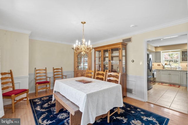 dining space featuring visible vents, crown molding, a wainscoted wall, light wood-style flooring, and a notable chandelier