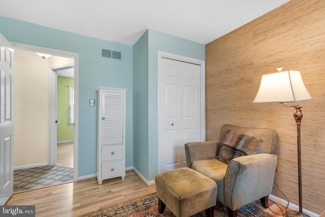 living area featuring baseboards, visible vents, wood finished floors, and an accent wall