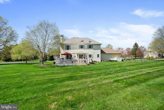 rear view of property with a chimney, a yard, and a deck