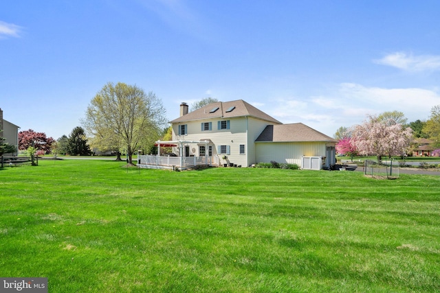 rear view of house featuring a yard, a pergola, a chimney, and a deck