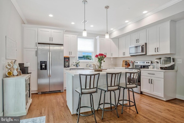 kitchen with appliances with stainless steel finishes, white cabinetry, light countertops, a center island, and a kitchen bar