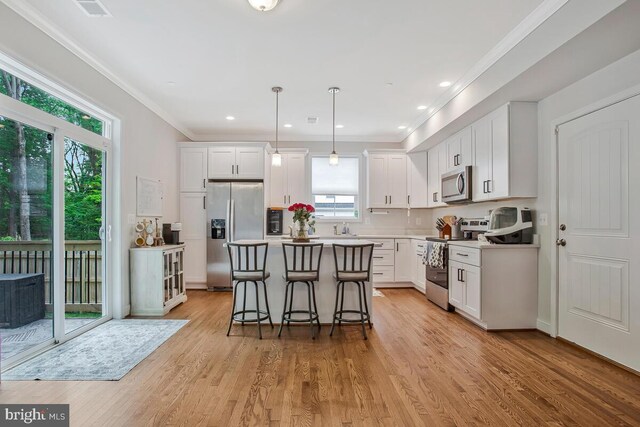 kitchen with appliances with stainless steel finishes, a breakfast bar area, a kitchen island, white cabinetry, and ornamental molding