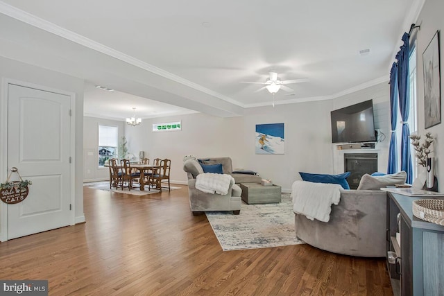 living room featuring dark wood-style floors, a chandelier, a ceiling fan, crown molding, and a glass covered fireplace