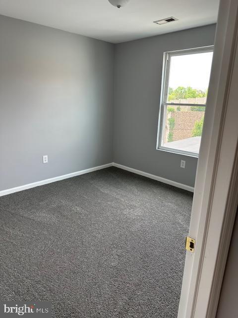 empty room with baseboards, dark carpet, and visible vents