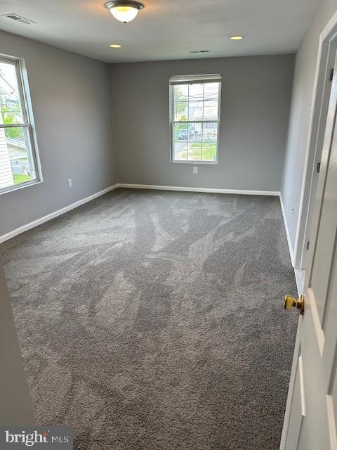 spare room featuring visible vents, baseboards, a healthy amount of sunlight, and dark colored carpet