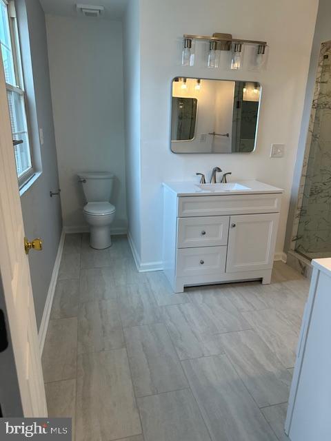 bathroom with visible vents, vanity, toilet, baseboards, and a stall shower