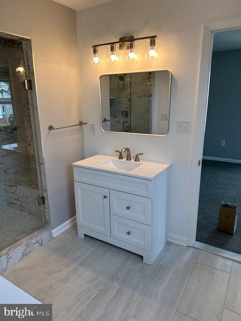 bathroom featuring baseboards, a marble finish shower, and vanity