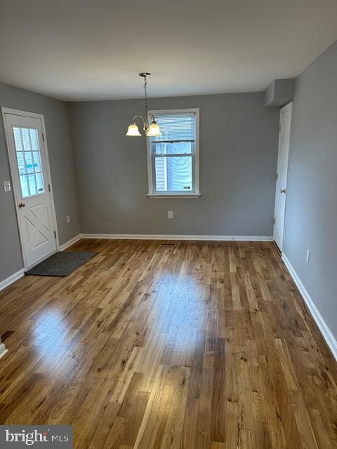unfurnished dining area featuring baseboards, an inviting chandelier, and wood finished floors