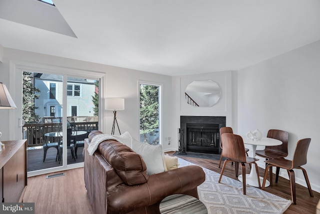 living room with baseboards, a fireplace with flush hearth, light wood-style flooring, and visible vents