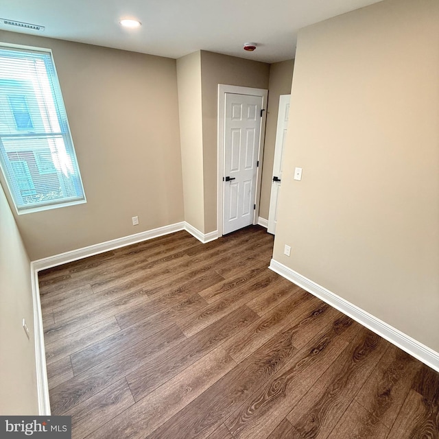 unfurnished room featuring baseboards, dark wood-style flooring, and visible vents