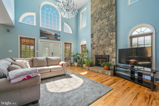 living area featuring a high ceiling, wood finished floors, a stone fireplace, and a chandelier