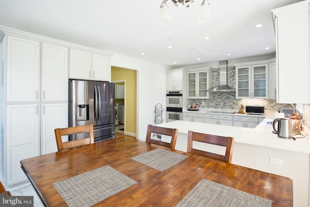 kitchen featuring stainless steel appliances, wall chimney exhaust hood, a sink, glass insert cabinets, and backsplash