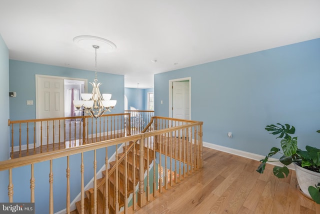 hall featuring an upstairs landing, a chandelier, wood finished floors, and baseboards
