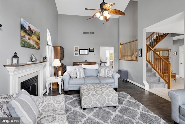 living area with ceiling fan, wood finished floors, high vaulted ceiling, baseboards, and stairs
