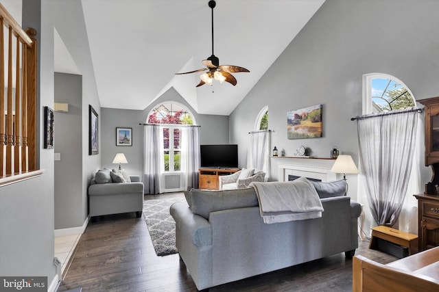 living area with high vaulted ceiling, baseboards, a ceiling fan, and wood finished floors