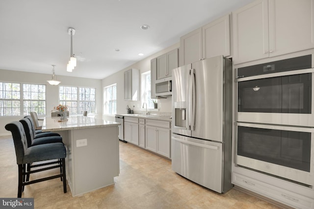 7438 Wildseed Pl, Hughesville, MD 20637 - kitchen featuring light stone counters, appliances with stainless steel finishes, a healthy amount of sunlight, and a kitchen bar