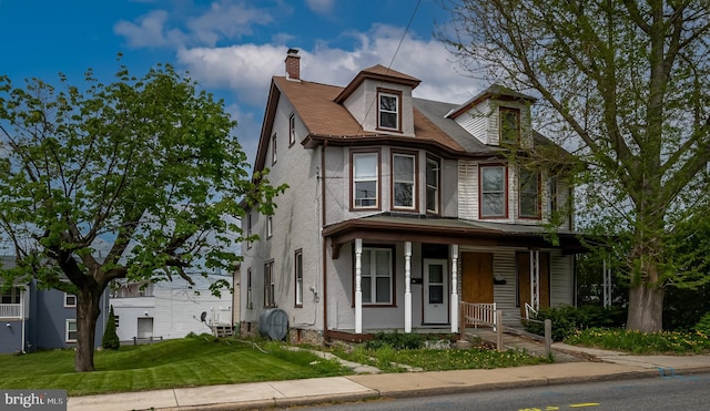 view of front of house with a chimney, stucco siding, covered porch, and a front yard