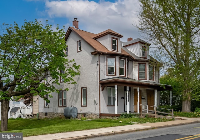 view of front facade featuring a porch, a chimney, heating fuel, and a front yard